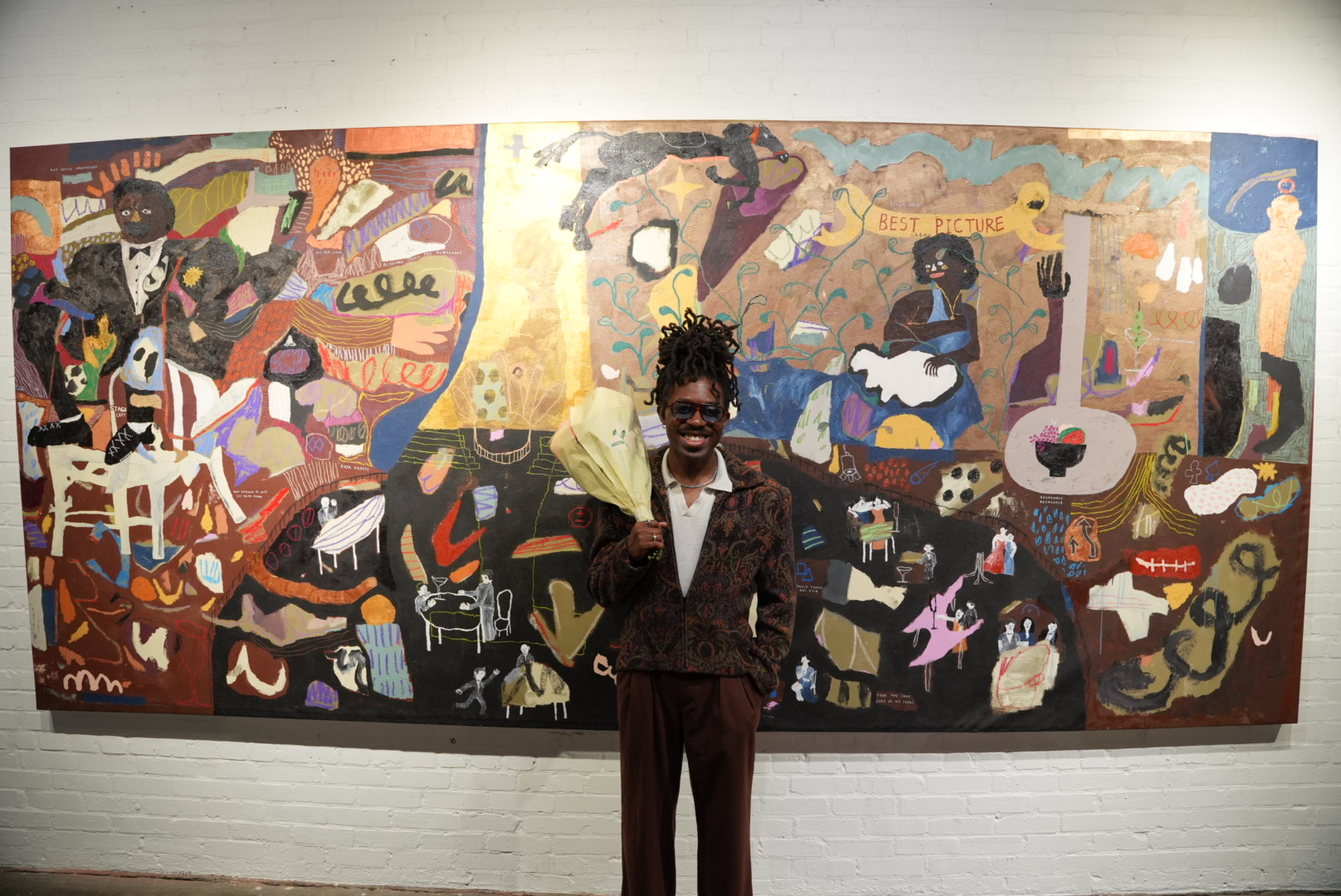 Bhare standing in front of a wall-length three-panel painting in a brick-walled space