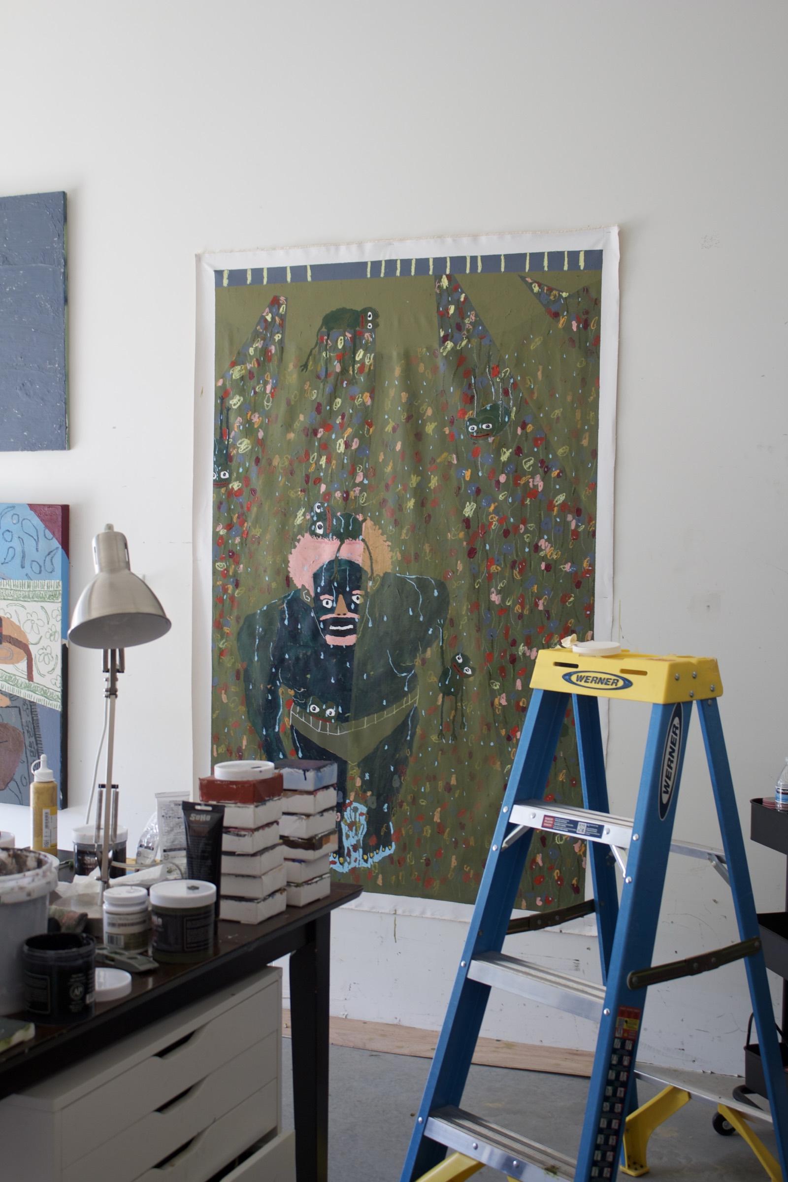 Bhare, "raining pepe" — a green canvas pinned to the studio wall beside a step ladder and a work table