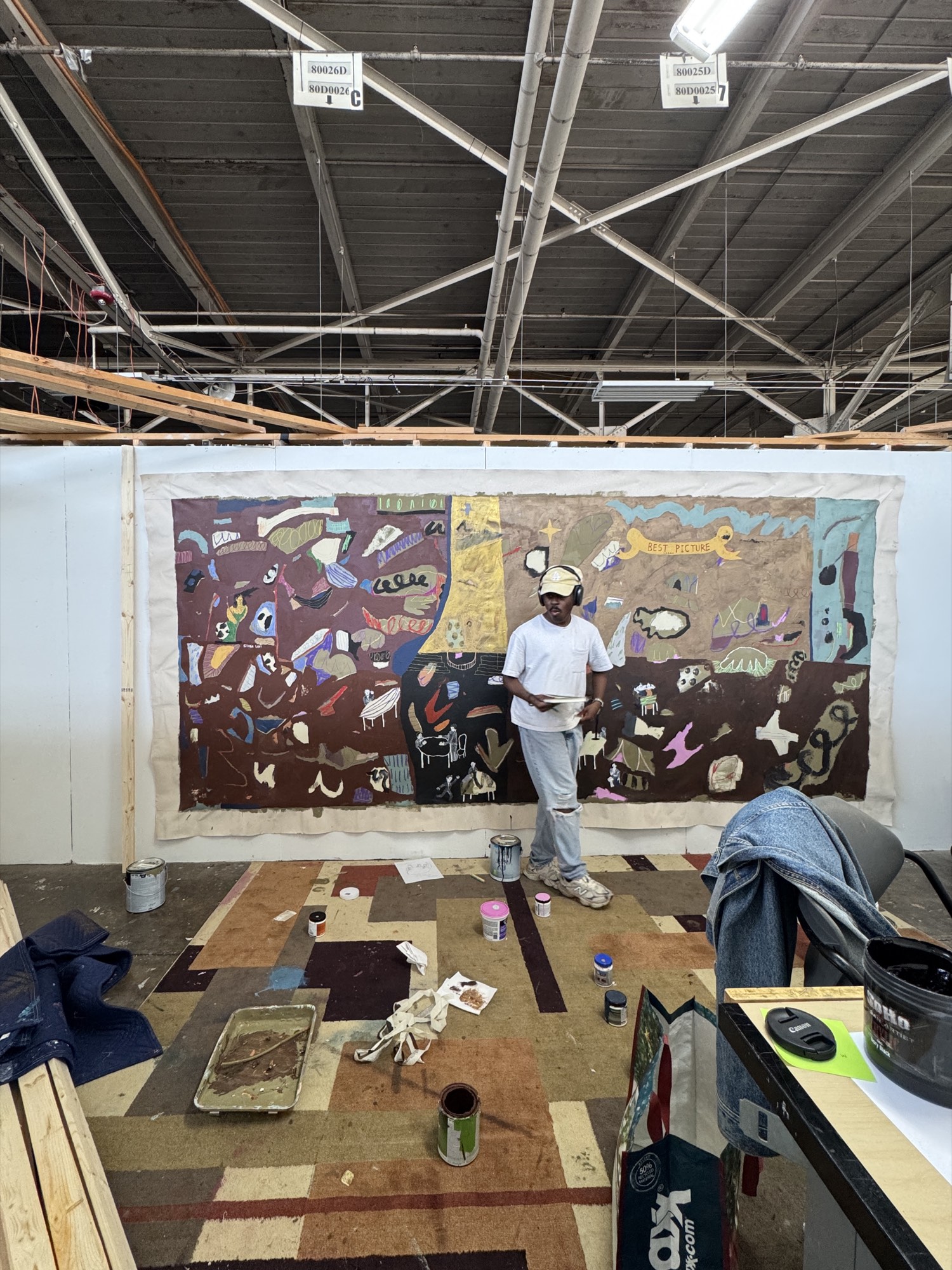 Bhare beside a floor-to-ceiling unstretched canvas in the studio, a small dog in the foreground